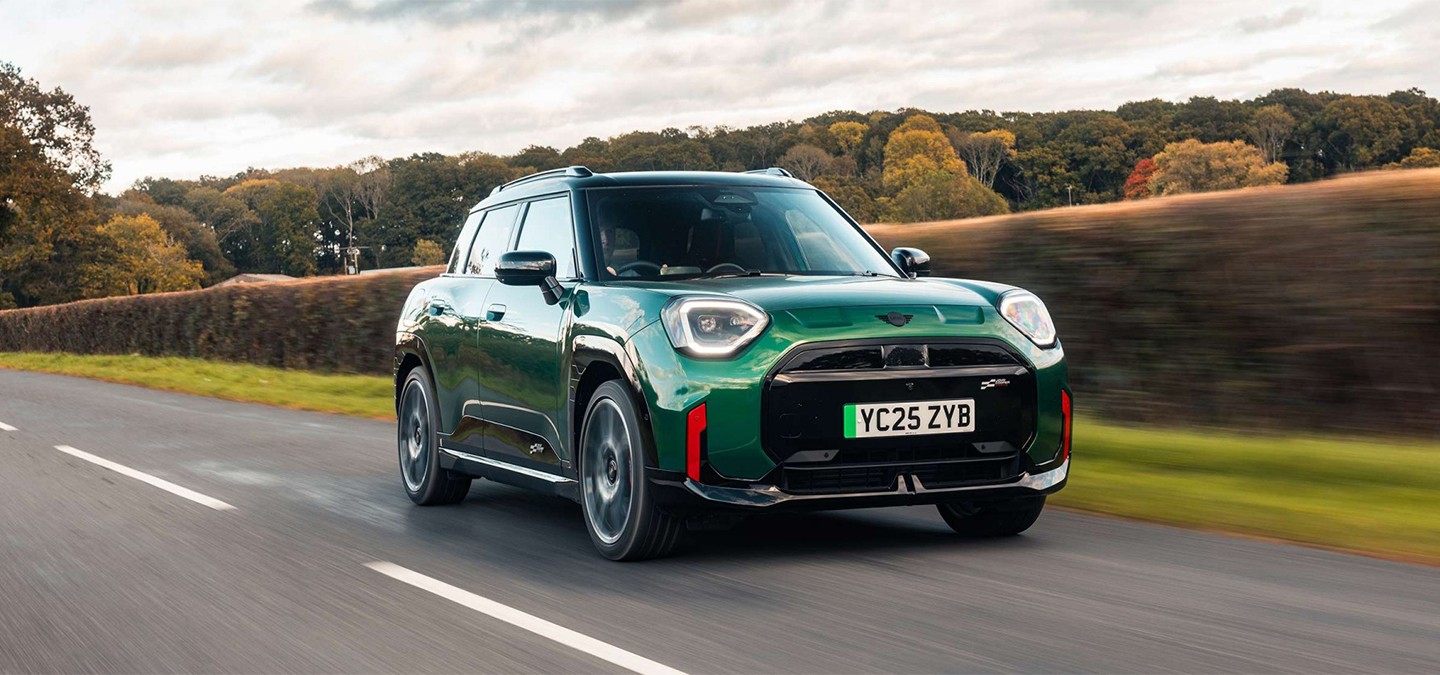 Front view of parking all-electric MINI Aceman in British Racing Green in car park with pink wall in the background